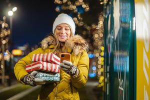 Femme avec manteau d’hiver, gants et tuque, tenant des paquets cadeaux et téléphone à la main